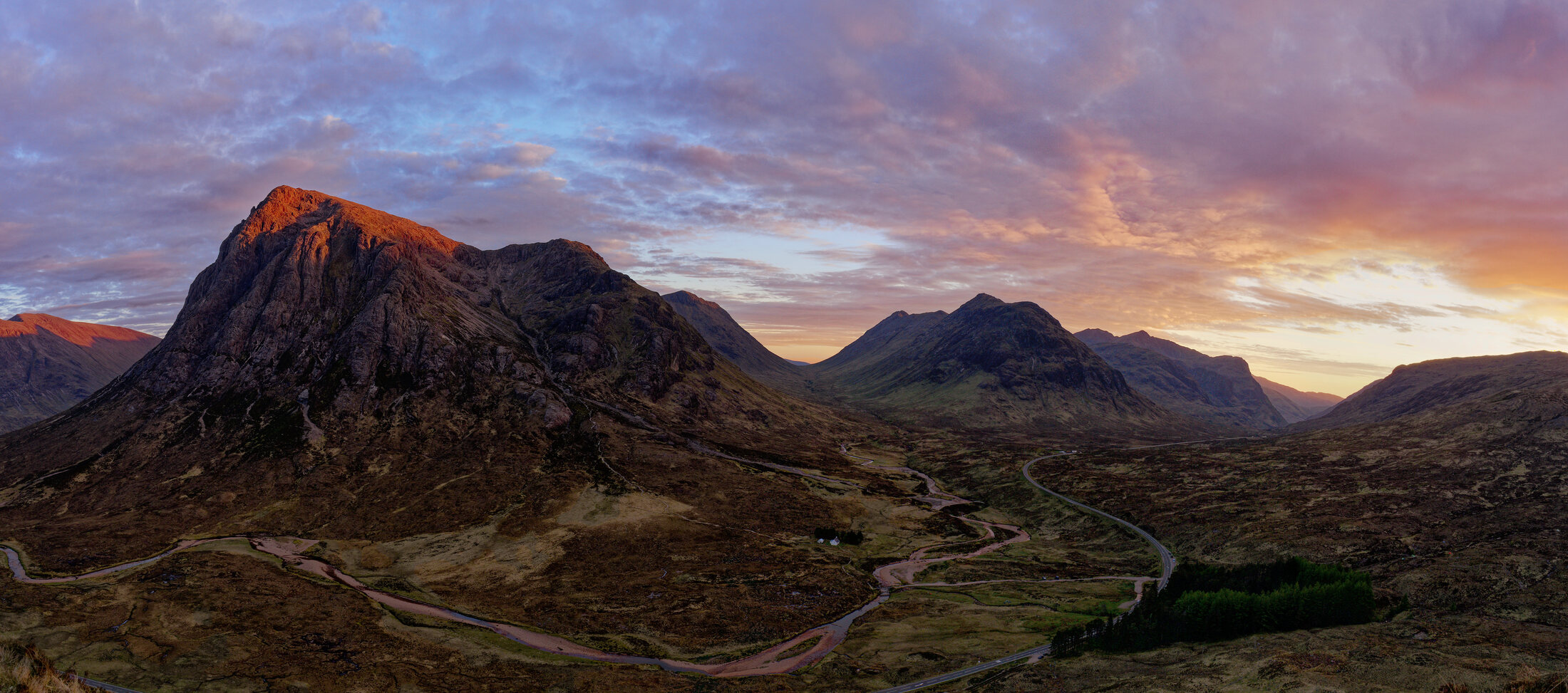 Mountain road winding through a remote valley beneath a fading sky.